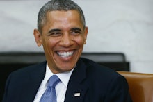 Barack Obama laughing in a black suit, white shirt and blue tie