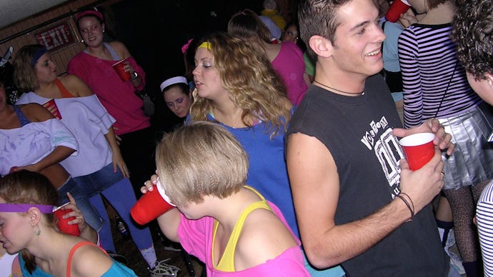A college party, with a group of girls dressed in 80s attire, all attendees drinking from red solo c...