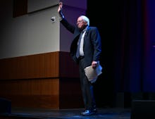 Bernie Sanders standing on stage with pages in his hand waving at latino voters