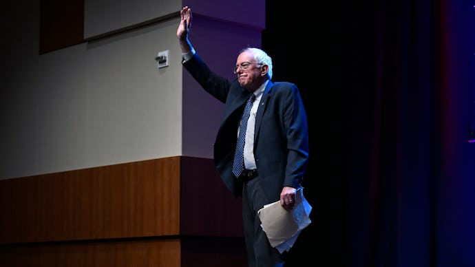 Bernie Sanders standing on stage with pages in his hand waving at latino voters