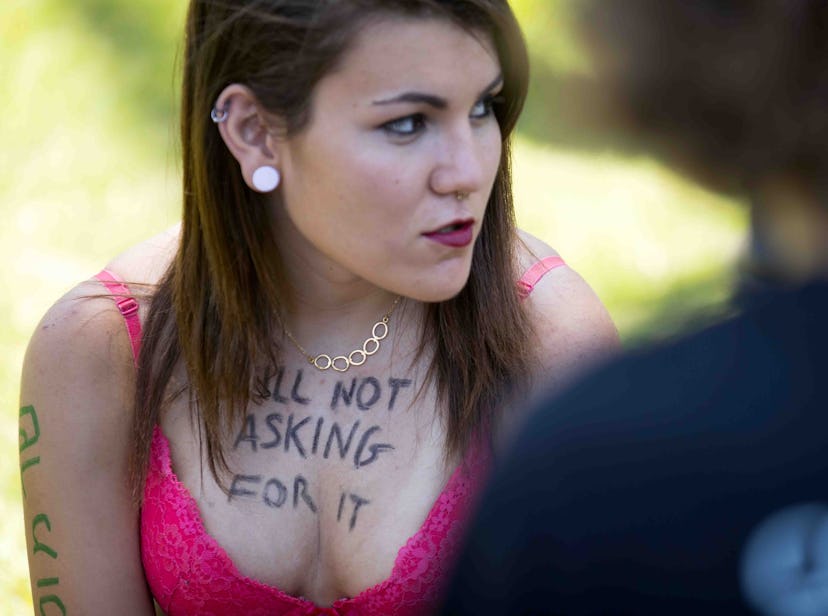 A teen brunette girl in a pink bra and a text on her chest 'Still not asking for it'