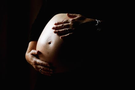 A pregnant woman in a dark room caressing her stomach