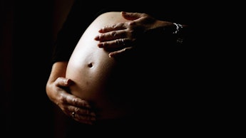 A pregnant  woman in a dark room caressing her stomach
