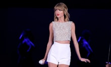 Taylor Swift performing on stage in a glitter beige top and white shorts