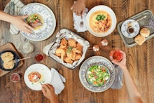 Chicken wings, soups, salad, and dips served in plates on a brown wooden surface