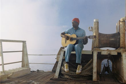 Seu Jorge sitting, holding a guitar
