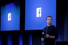 Mark Zuckerberg standing on stage delivering a speech with the facebook logo behind him