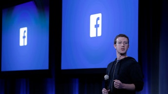 Mark Zuckerberg standing on stage delivering a speech with the facebook logo behind him