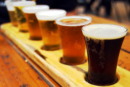 A wooden beer holder with six cups of beer on a wooden surface