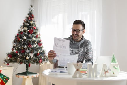 A man smiling and holding a form and ready to apply for a new job next to a Christmas tree