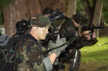 Soldiers in a forest aiming their guns at something in the distance