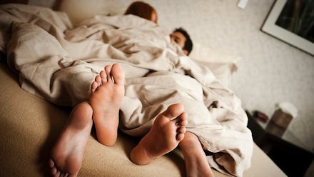 Two people lying in a bed covered with a blanket, who use a new dating app that lets them track thei...