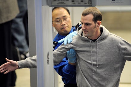 A TSA agent pats down a man in a grey sweatshirt at the airport