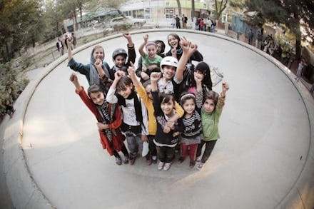 A group of Afghan children whose lives have been changed through skateboarding posing and waving wit...