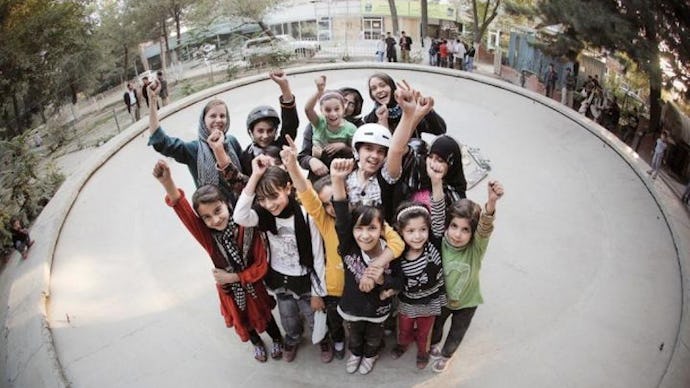 A group of Afghan children whose lives have been changed through skateboarding posing and waving wit...