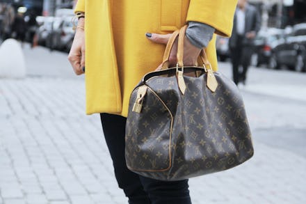 A woman in a yellow jacket holding a leather designer purse