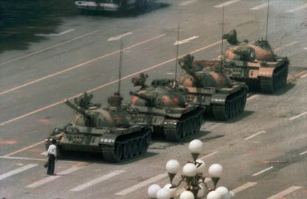 Man in white shirt and black jeans standing in front of four tanks at the Tiananmen Square