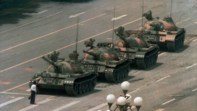 Man in white shirt and black jeans standing in front of four tanks at the Tiananmen Square