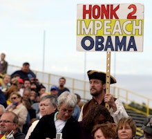 A man holding a big "honk 2 impeach Obama" paper with a wooden stick