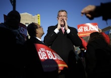 Bill De Blasio standing in the center of the crowd while people around him hold up red signs with hi...