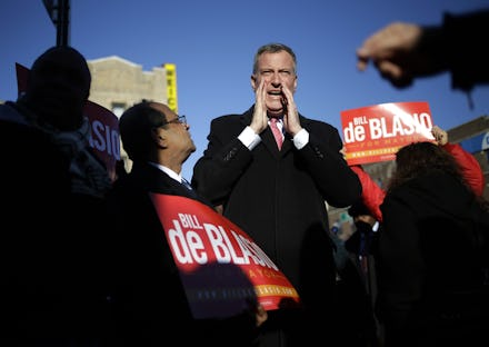 Bill De Blasio standing in the center of the crowd while people around him hold up red signs with hi...