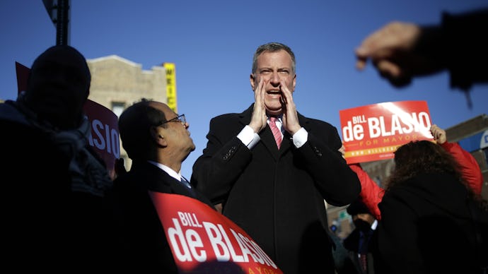 Bill De Blasio standing in the center of the crowd while people around him hold up red signs with hi...
