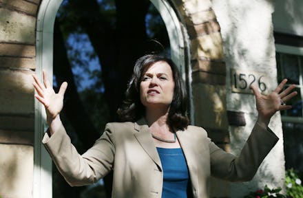 A woman standing outside of a building on a sunny day with her arms held up and her eyes closed