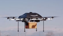 A black Amazon drone in the air, delivering a package