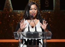 Shonda Rhimes wearing a white gown while giving a speech on stage