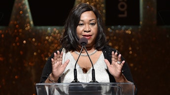 Shonda Rhimes wearing a white gown while giving a speech on stage