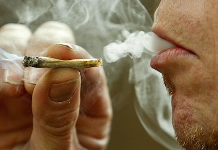 A closeup of a man's mouth smoking a marijuana joint and exhaling the smoke 