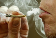 A closeup of a man's mouth smoking a marijuana joint and exhaling the smoke 