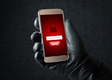 A man's hand in a black leather glove holding a phone with a red alarm notification about theft and ...