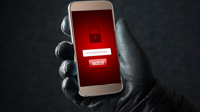 A man's hand in a black leather glove holding a phone with a red alarm notification about theft and ...