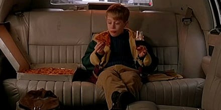 Macaulay Culkin eating pizza and drinking coke in the back seat of a car.