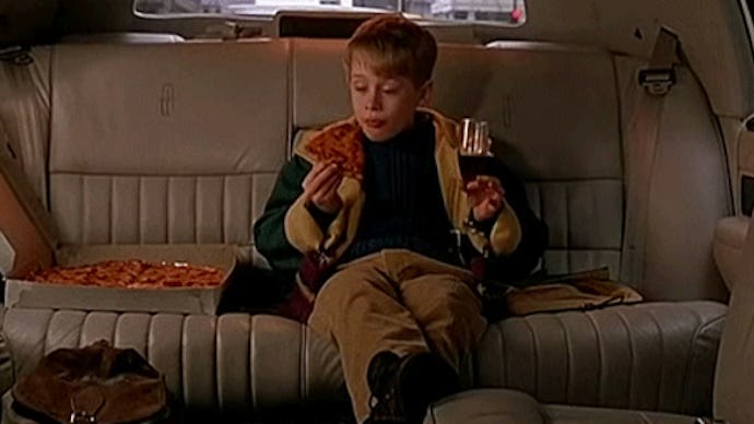 Macaulay Culkin eating pizza and drinking coke in the back seat of a car.