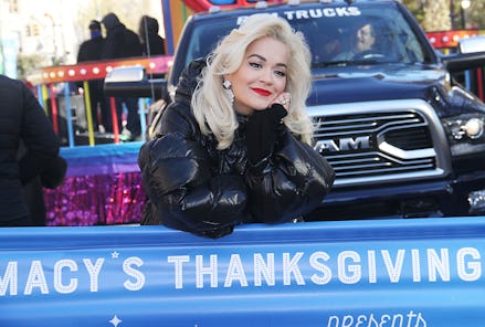 Rita Ora standing in front of a large truck and behind a macy's thanksgiving sign