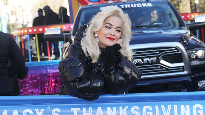 Rita Ora standing in front of a large truck and behind a macy's thanksgiving sign