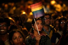 LGBT activists in India protesting for their rights, one is in focus holding a flag with pride color...