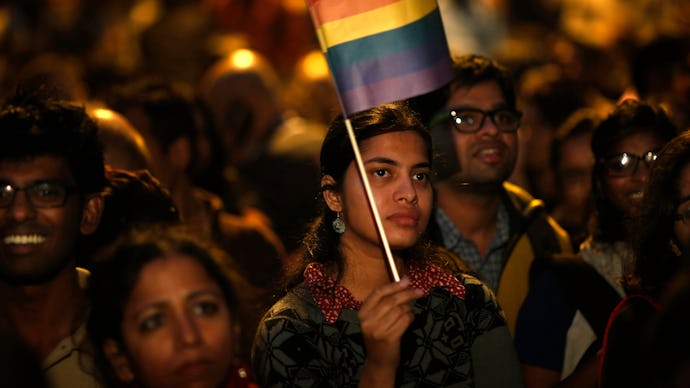 LGBT activists in India protesting for their rights, one is in focus holding a flag with pride color...