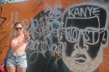 A woman posing in front of a large Kanye West mural on an orange wall