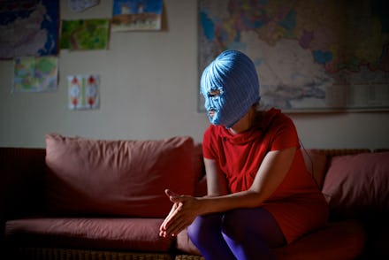 A member of the Russian punk group Pussy Riot wearing a blue mask and a red shirt while sitting on a...