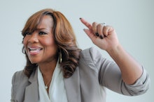 Mona Scott-Young in a grey blazer and white blouse, pointing at something passionately 