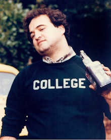 John Belushi in a black sweater with 'College' print on it