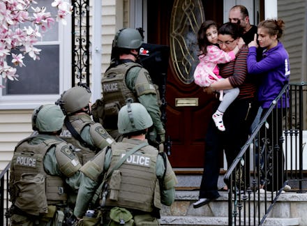 Four police officers entering a house with a woman holding a child at the entrance and another child...