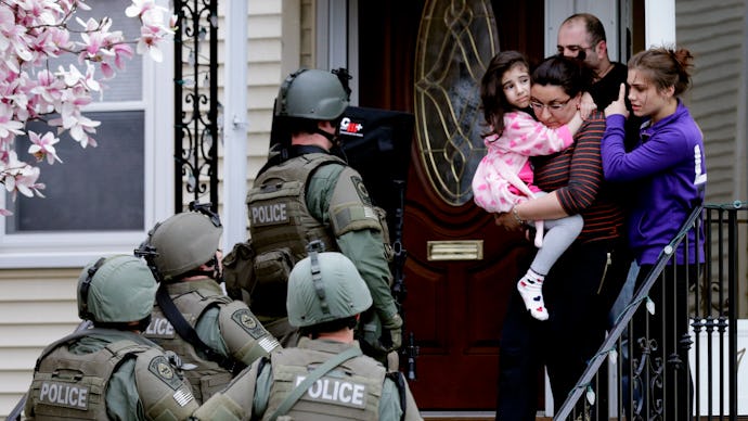 Four police officers entering a house with a woman holding a child at the entrance and another child...