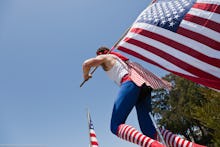 A man riding a unicycle in a white tank, blue pants and striped red and white socks, with an America...