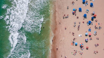 A crowded beach next to the sea from an aerial view