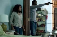 A scene from No Good Deed where Idris Elba is pointing a gun while a woman hides from him behind a w...