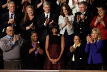 Michelle Obama standing and smiling while the people around her clap